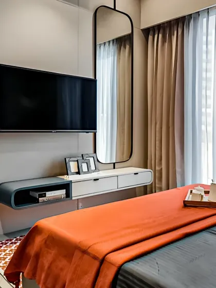 We designed this compact bedroom with a floating TV console that doubles as a vanity. The minimalist, curved design in white and grey saves floor space, while the long mirror enhances the room's sense of spaciousness.