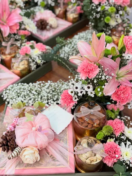 A closer view of the Roka favors, highlighting the fresh lilies and carnations. The gifts are elegantly wrapped and paired with jars of almonds and cashews, making for a classic and thoughtful gesture.