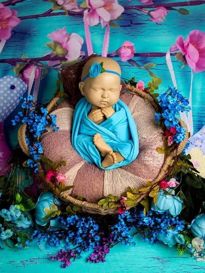 A serene newborn portrait with the baby swaddled in blue, resting in a nest decorated with blue flowers and charming bird props. The bright blue background makes this a cheerful and lovely keepsake.
