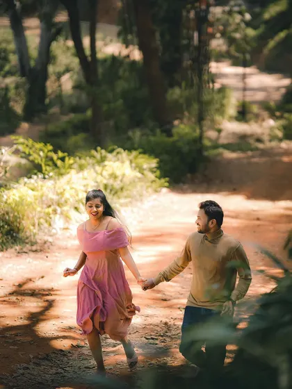 A romantic shot of a couple walking hand-in-hand down a sun-dappled path.