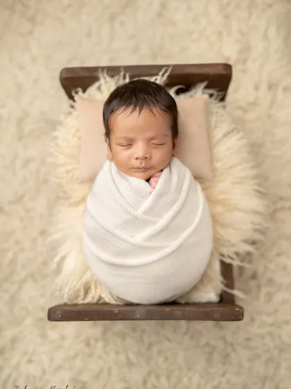 A classic portrait of a swaddled newborn, resting peacefully on a tiny bed. These are the timeless images you will cherish forever.