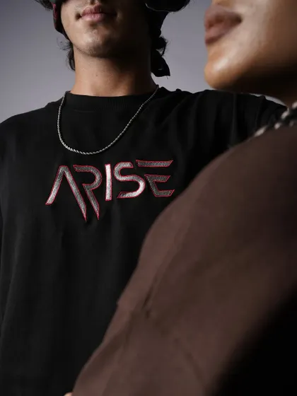 An artistic, close-cropped shot focusing on the embroidered 'ARISE' logo. The image creates a sense of intimacy and intrigue, drawing attention to the brand name.