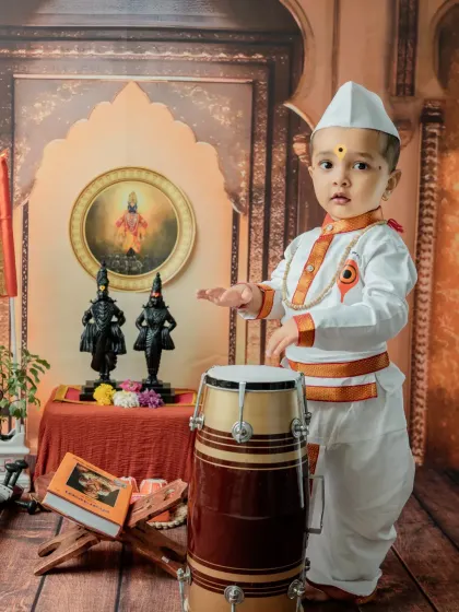 A classic pose with the baby standing by the pakhawaj drum. This full-length shot showcases the complete traditional Varkari outfit.