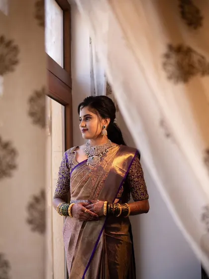 A candid shot of the bride Divya, looking out the window. The natural light beautifully catches the shimmer on her saree and the subtle glow of her makeup.