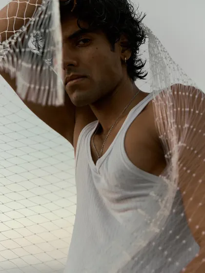 A close-up portrait using a fishing net to frame the face. This adds a layer of texture and narrative to the shot, hinting at a story connected to the sea.
