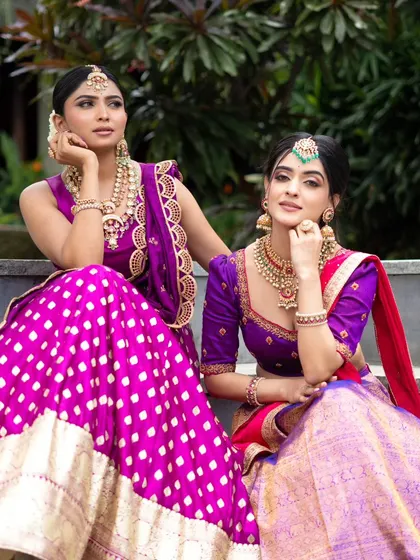 A candid moment between models wearing our purple and pink half sarees, showing the joy and elegance of our traditional wear collection.