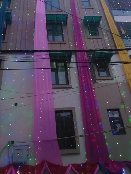 A multi-story building decorated with long, flowing drapes in various colors, illuminated by strings of lights.