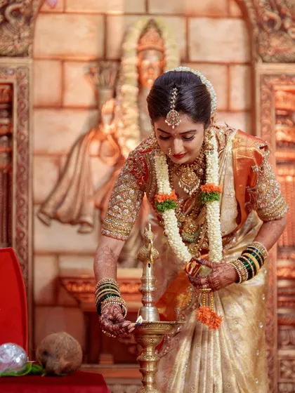 A traditional moment of lighting the lamp. The rich gold and red of her bridal blouse shine in this photo, showcasing the detailed craftsmanship.