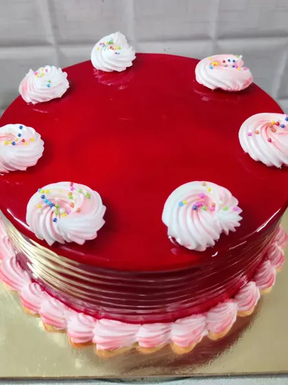A strawberry cake with a glossy red glaze. The simple piped rosettes are topped with colorful sprinkles.