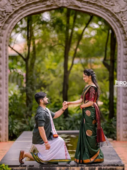 A classic proposal pose in a garden setting. The couple's traditional green and red outfits look beautiful against the lush, natural backdrop.