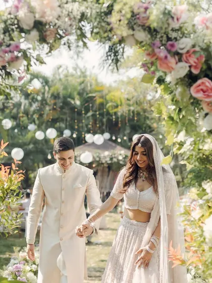 A couple walks through a garden path lined with floral arches, creating a fairytale-like experience.