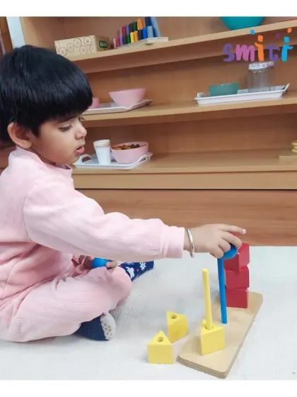 A toddler carefully stacks colorful blocks, an activity that develops hand-eye coordination and an understanding of size and balance. Even our youngest learners are engaged in purposeful play.
