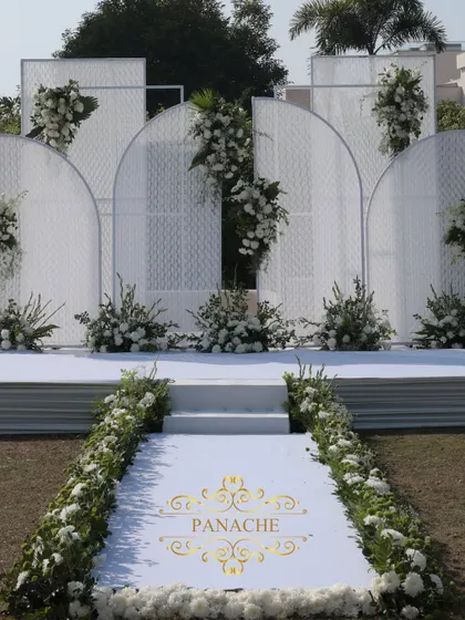 The stunning all-white stage, featuring modern arched panels and asymmetrical floral arrangements. It's a perfect example of contemporary and elegant event design.
