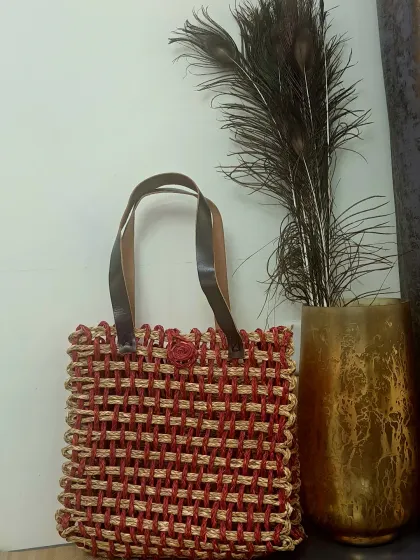 This unique tote bag features an open-weave design with red and natural fibers, finished with durable leather straps. It's a modern, artistic take on the traditional woven bag.