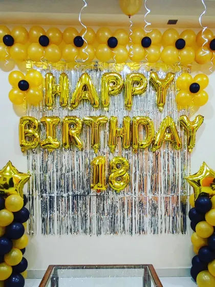 An 18th birthday celebration with a striking yellow and black theme. The decoration features a 'Happy Birthday' foil banner, balloon pillars with star toppers, and a flower-like balloon garland across the top.