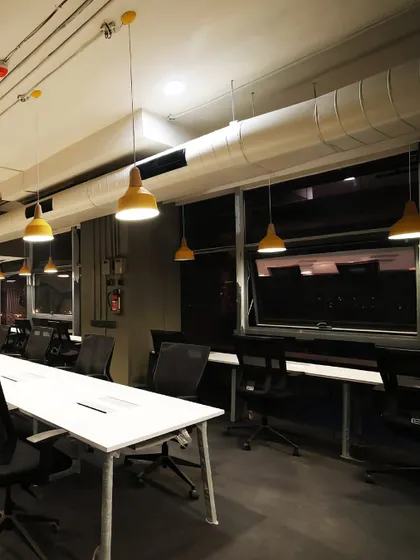 A focused work zone at Innov8 with a long desk and yellow pendant lights. The industrial aesthetic, with exposed ductwork, is softened by the warm lighting, creating a space conducive to productivity.