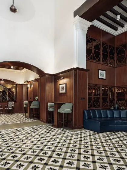 A curved navy blue sofa sits against custom wood-paneled walls, creating a sophisticated lounge area within The Bangalore Club. The design respects the original architecture while introducing contemporary furniture for comfort and style.