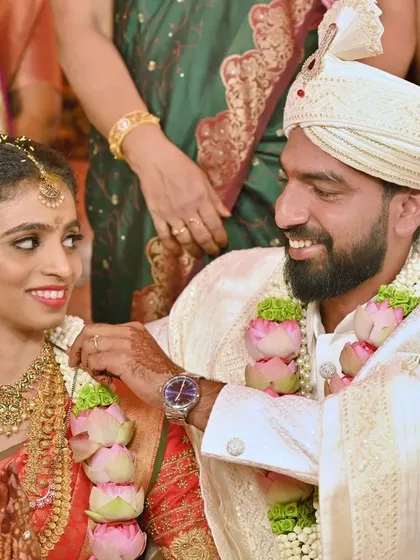 Capturing the candid expressions during the wedding ceremony, this photo shows the groom lovingly adjusting the bride's garland.