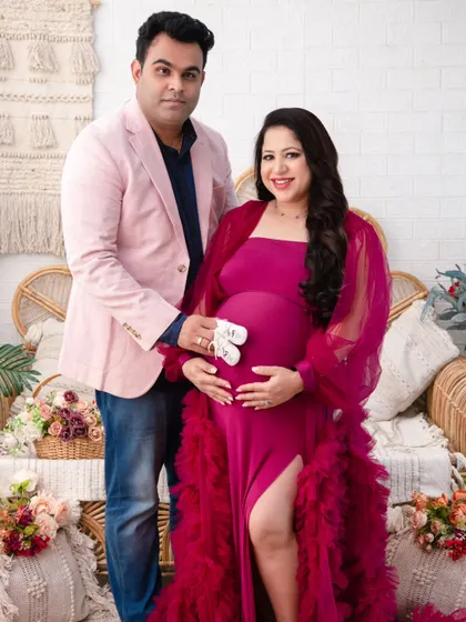 A classic portrait of the couple, proudly holding a pair of baby shoes. The vibrant magenta gown adds a pop of color and joy to the image.