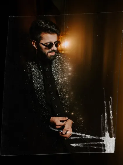 A cool, edgy portrait of the groom in his sparkling Sangeet jacket and sunglasses, captured with an artistic foreground effect.