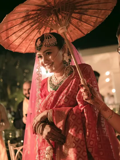 The bride's joyful entrance under a traditional umbrella, her smile lighting up the moment.