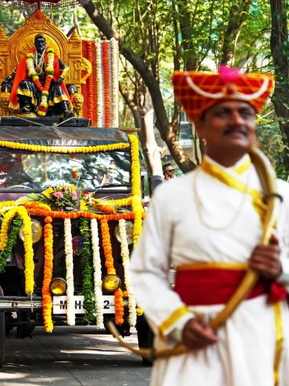 A man dressed in traditional attire as a Mavala, or soldier, walks ahead of the procession float. This photo highlights the historical and cultural elements of the parade.