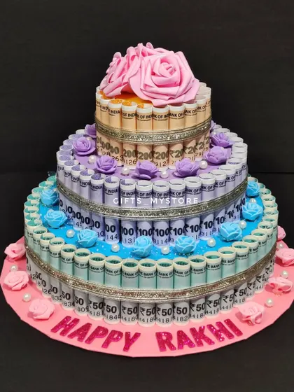 A beautiful three-tier money tower cake with a "Happy Rakhi" message, perfect for spoiling your sister.