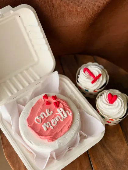 Celebrate a one-month anniversary with this sweet pink and white combo. The bento cake says "one month" and is paired with two cupcakes topped with the number '1' and a heart.