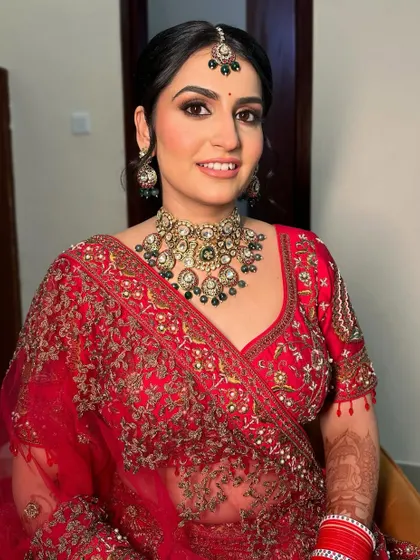 This regal bridal look is all about timeless grace. The makeup features a classic smokey eye and a perfectly sculpted base to complement the rich red outfit and heavy jewelry.