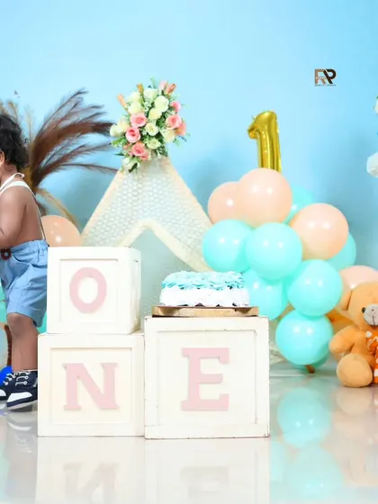 A playful moment from a first birthday session, with the birthday boy interacting with the balloons. The soft pastel colors create a gentle and celebratory mood.