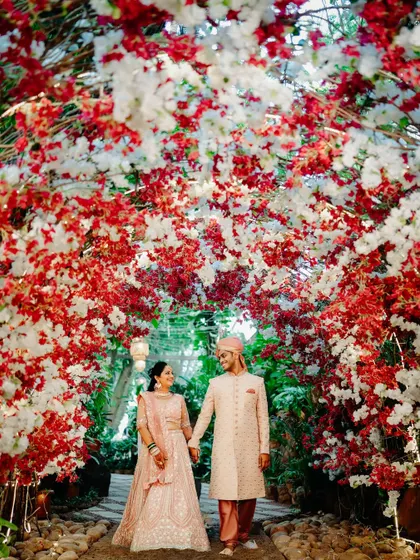A romantic portrait of the couple framed by a stunning red and white floral arch. The way they look at each other captures the magic of the moment.