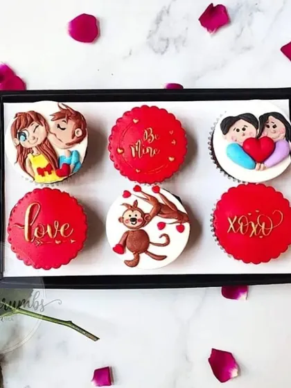 A box of custom Valentine's Day cupcakes with assorted fondant toppers. The designs include cute couples, love messages, and a cheeky monkey.