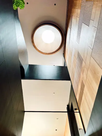 This staircase atrium is defined by a striking contrast of black-stained oak and white oak paneling. A circular skylight at the top introduces a dramatic column of daylight, transforming the stairwell into a sculptural, light-filled void.