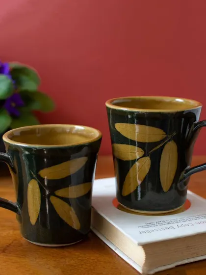 A closer view of the black and gold Lantana mugs. You can see the texture of the glaze and the hand-painted quality of the leaf design, showcasing the skill of the artisan.