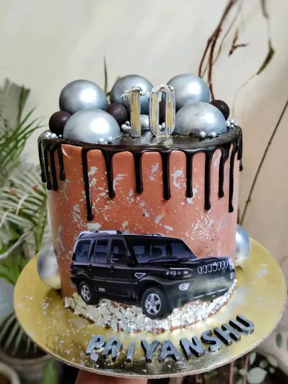 For the car lover, a cake featuring their favorite ride. This chocolate Oreo cake has silver sphere details, chocolate drips, and a silver road for the car.