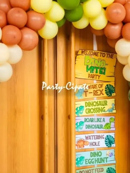 A dinosaur-themed direction sign and balloon arch at the entrance. The signs point to the 'Watering Hole' and 'Dino Egghunt', adding a fun, interactive element to the party.