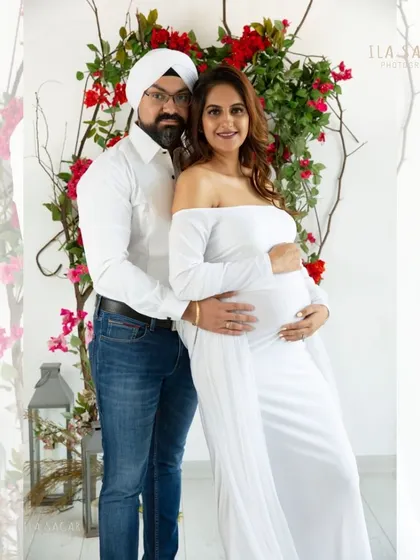 A lovely couple's portrait during their maternity session. They stand together in front of a floral arch, sharing a happy moment as they anticipate their baby's arrival.