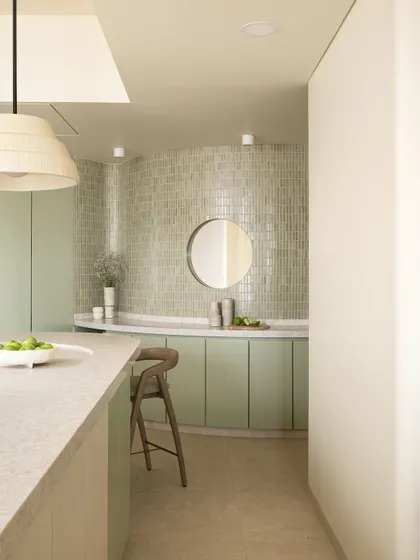 A view of the coffee corner in the same kitchen, with a curved counter, mint-green mosaic tiles, and a circular mirror.