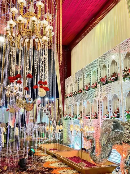An opulent decor setup with a cascade of hanging crystals and flowers in front of a traditional Rajasthani jharokha wall.