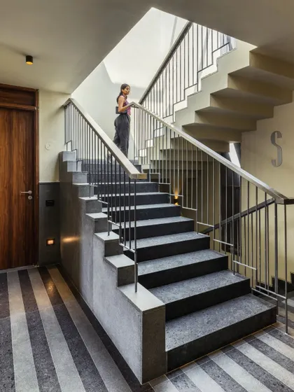 The central staircase is flooded with natural light from a skylight above, making the transition between floors a bright and pleasant experience. The simple steel railing and stone steps maintain the building's clean, modern aesthetic.