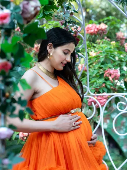 A close-up shot of a mom-to-be in an orange gown, framed by flowers. This portrait highlights her happy expression and the beautiful details of her look.