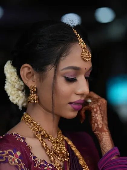 A beautiful profile shot. This highlights the soft purple eyeshadow, the elegant updo with fresh flowers, and the intricate gold jewellery.