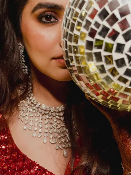 A creative shot of the bride on her Sangeet night, her face partially hidden by a disco ball, reflecting the glamorous and fun-filled theme of the party.