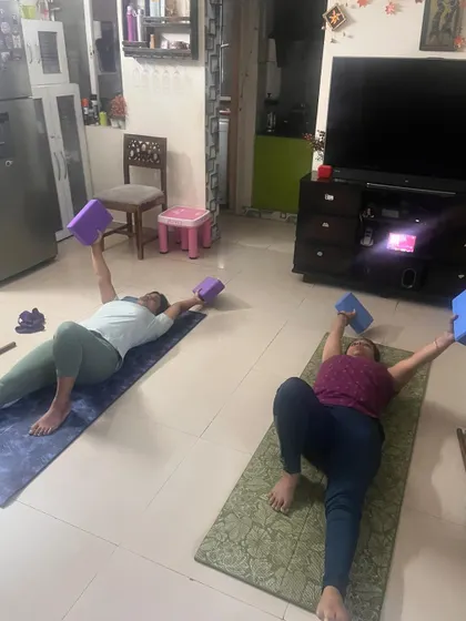 Two clients hold a floor press position using yoga blocks, an exercise that builds chest and core strength. This demonstrates our use of props to enhance bodyweight exercises.