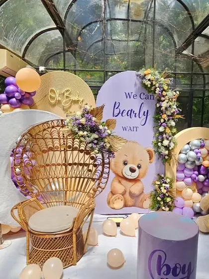 A detailed view of the 'We Can Bearly Wait' baby shower stage, highlighting the teddy bear, wicker chair, and custom backdrops.