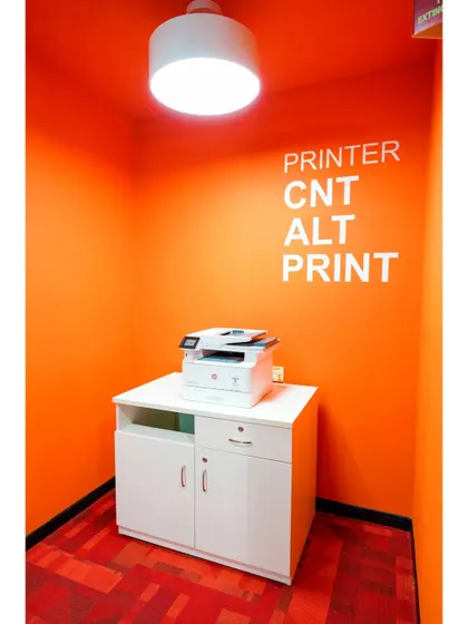 Even functional spaces like the printer room are given a design treatment. A bold orange color and playful text "CNT ALT PRINT" make a mundane task more enjoyable.