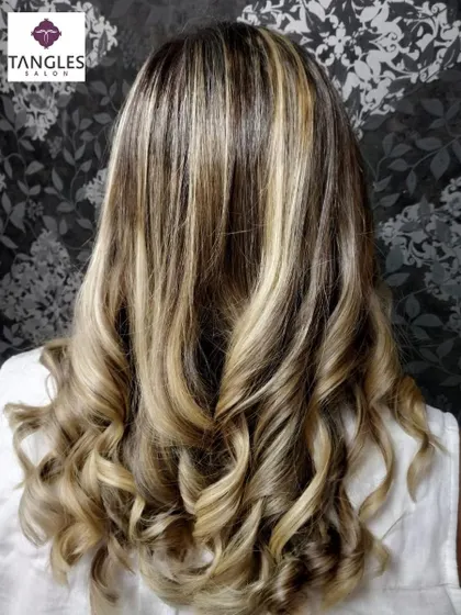 This back view showcases the full effect of the golden blonde highlights on curled hair, creating a high-contrast, dimensional style.