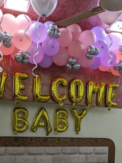 A close-up of the 'Welcome Baby' gold foil letters and the colorful balloon arrangement on the ceiling above the bed.