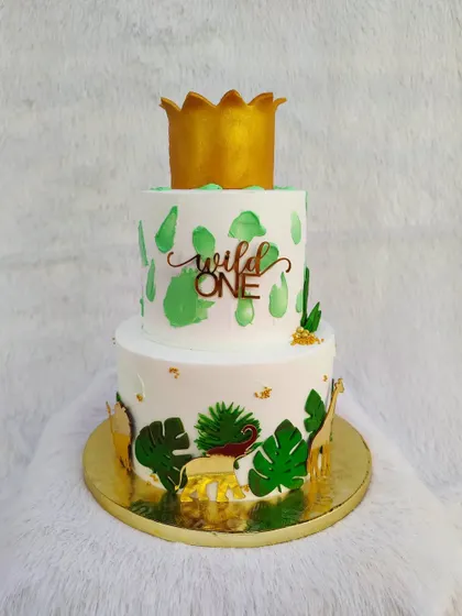 A "Wild One" jungle theme cake. This two-tier design uses animal silhouettes and tropical leaves for a more modern and stylish take on the safari theme.