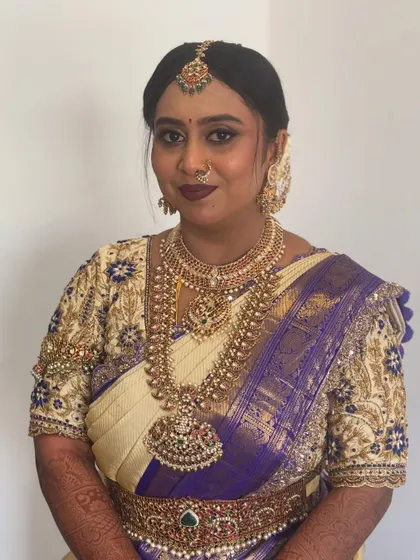 A beautiful bride in a traditional white and purple silk saree, with her hair neatly styled to complement her temple jewellery.